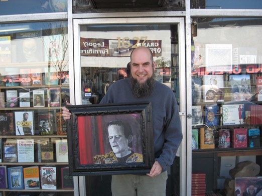 Footnote Books owner Troy Beaver outside his store holding Shel's painting of Frankenstein's Monster.